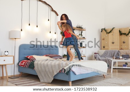 Happy young mother and cute little daughter holding hands, dancing, jumping on bed, laughing mum playing with excited adorable preschool child in bedroom, funny family activity at home, having fun
