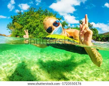 Woman sunbathing on floating an air beach mattress with a surgical mask during Covid-19. Blonde woman having a bath in tropical sea in coronavirus quarantine. Holidays travel in COVID pandemic. Royalty-Free Stock Photo #1723550176