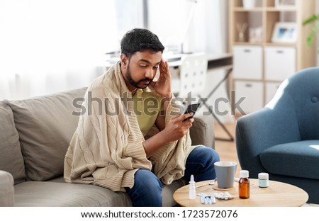 health, cold and people concept - sick young indian man in blanket with smartphone at home Royalty-Free Stock Photo #1723572076