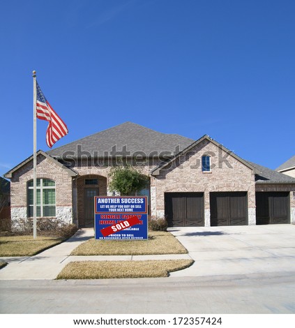 American Flag Sold Real Estate Sign suburban ranch style home blue sky residential neighborhood USA