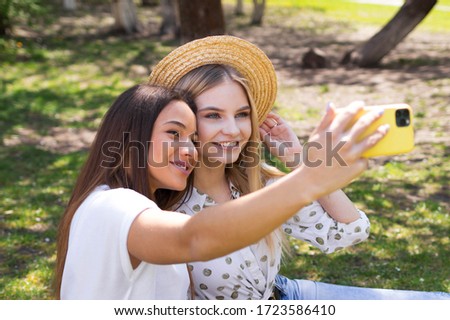 Two girlfriends of the blogger take selfies on the phone, the girls are photographed in the park