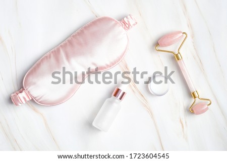 Sleeping eye mask, serum dropper bottle, moisturizer cream, face massage roller on marble background. Nighttime skincare routine concept Royalty-Free Stock Photo #1723604545