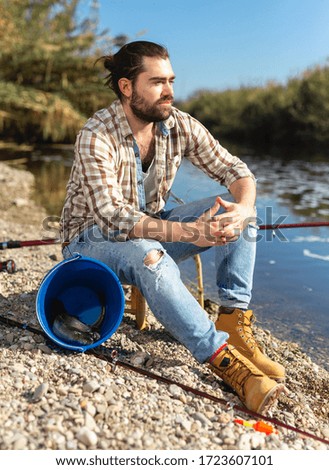 Positive adult man with rod relaxing and enjoying fishing by lakeside 