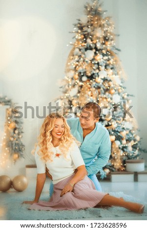Vertical picture of smiling happy young married couple wife and husband sitting near christmas tree with christmas lights around. Boyfriend and girlfriend in xmas new years eve together. Love, trust