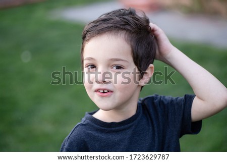 Portrait of a cheerful child. 6 years old kid scratching head with his hand, smiling. Thick hair. Concept of challenge, interest, idea, communication, treatment of lice, caring for a child. 
