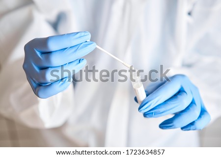 Doctor holding swab test tube for 2019-nCoV analyzing. Coronavirus test. Blue medical gloves and protective face mask for protection against covid-19 virus. Coronavirus and pandemic. Royalty-Free Stock Photo #1723634857