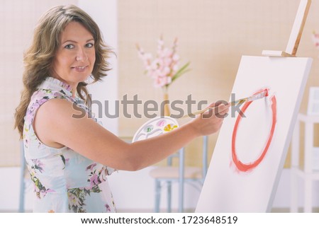 Woman artist holding palette with different paints and paintbrush in a workshop studio.
