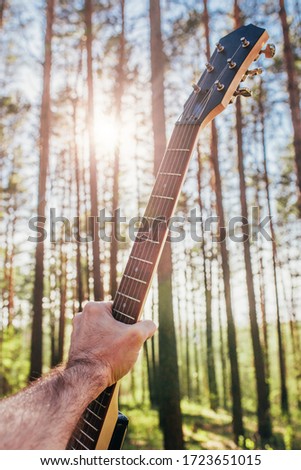 Guitar in a man hand against a blue sky - sunbeams through the trees - open-air rock festival