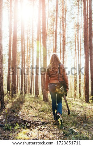 A slender girl in jeans and a jacket with a guitar in the forest - freedom and rock music - an outdoor music festival - open air
