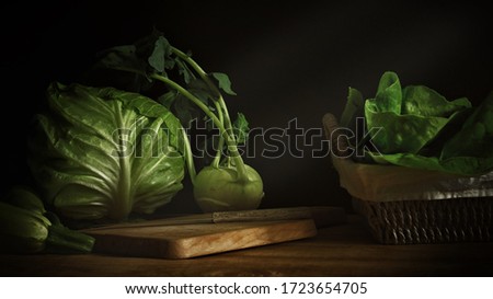 Close up of fresh green vegetables kohlrabi turnip cabbage and zucchini on wooden table and wooden chopping board in low light photography
