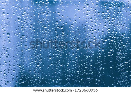 rain drops on a blue window glass transparent surface. water droplets on windowshield in a rainy days in autumn spring summer winter in night. stormy weather. loneliness sad depression concept.