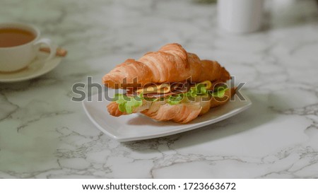 Close up view of a plate of breakfast meal with croissant sandwich ham and cheese on marble desk 