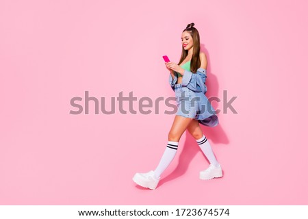 Full size profile photo of pretty lady hold telephone texting friends walk street wear denim jacket green crop top mini shirt long socks shoes isolated pastel pink color background