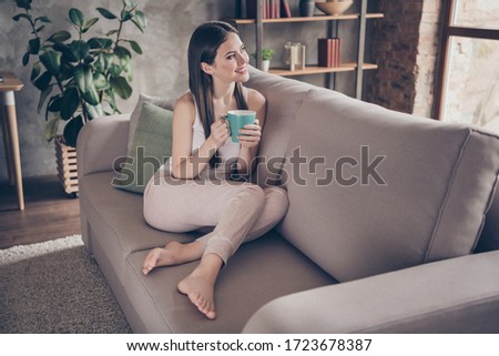 Full size photo of candid content girl sit divan have holiday hold cup coffee look dream future life weekend plan in house indoors apartment