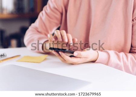 Young woman using mobile phone while working at home with laptop. 