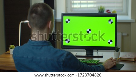 Male Video Editor Works on His Personal Computer with Big Green Screen Mock Up Display.