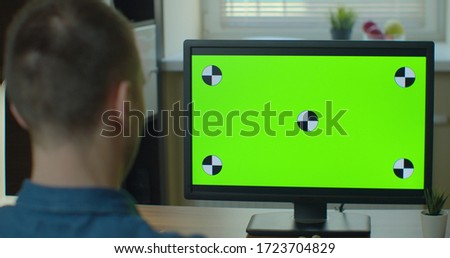 Creative Designer Sitting at His Desk Uses Desktop Computer with Two Green Mock-up Screens.