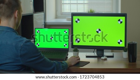 Designer Sitting at His Desk Uses Desktop Computer with Green Mock-up Screen.