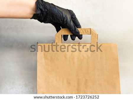 A woman's hand in a black protective glove holds a craft bag. Concept of eco-friendly and safe shopping during the coronavirus pandemic. Close-up, selective focus