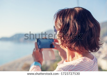 Attractive retired woman 50-60 years old travels and takes photos on a smartphone at the viewpoint while traveling