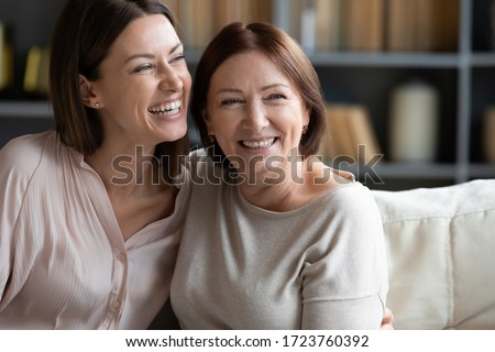 Happy mature mother and adult daughter hugging close up, having fun, sitting on couch at home, smiling woman embracing older mum, spending leisure time together, two generations good relationship Royalty-Free Stock Photo #1723760392
