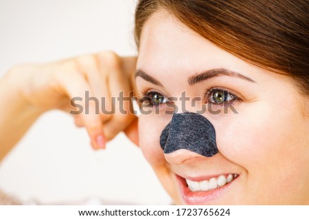 Woman appying clear-up strips on nose, using pore cleansing textile mask, on white. Girl taking care of skin complexion. Beauty treatment. Skincare.