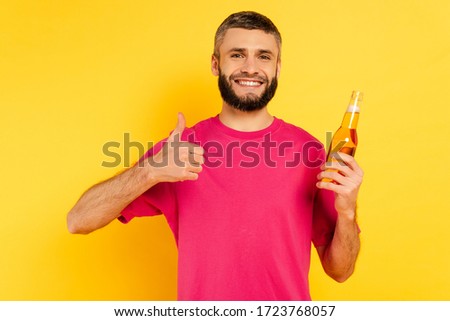 happy bearded guy in pink t-shirt showing thumb up with beer on yellow