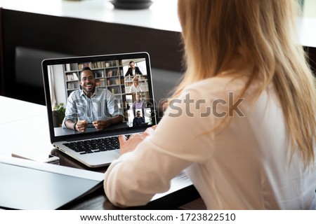 Back view of businesswoman sit at desk talk on video call with multiracial colleagues, woman employee speak have webcam conference on laptop with diverse coworkers, online briefing with team Royalty-Free Stock Photo #1723822510