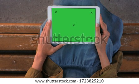 Lady holding tablet while sitting on a bench.