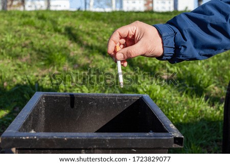 The hand throws the cigarette into the trash