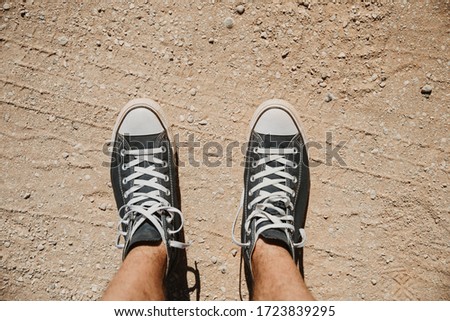 Top view of male legs on sand dirt road or desert dry land. A pair of dirty blue sneakers with white shoelaces. Feet and sport shoes of a tourist, traveler or globetrotter Royalty-Free Stock Photo #1723839295