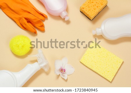 Plastic bottles of dishwashing liquid, glass and tile cleaner, detergent for microwave ovens and stoves, rubber gloves, garbage bags and sponges on a beige background. Top view. Cleaning set.