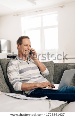 selective focus of cheerful freelancer talking on smartphone and using laptop at home