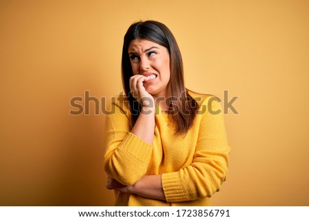 Young beautiful woman wearing casual sweater over yellow isolated background looking stressed and nervous with hands on mouth biting nails. Anxiety problem.