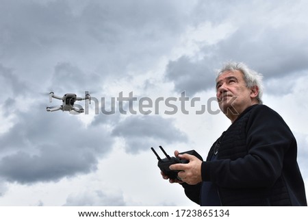 Senior man with remote control navigates a drone in the cloudy sky. Retired person leisure activity. Elderly man navigates unmanned aerial vehicle. 
