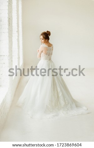bride in white wedding dress. happy beautiful young woman in white traditional wedding dress on white background. big windows and white walls.