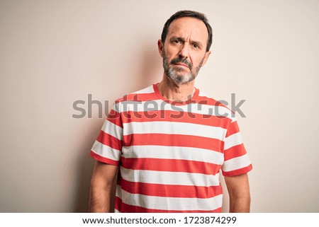 Middle age hoary man wearing casual striped t-shirt standing over isolated white background Relaxed with serious expression on face. Simple and natural looking at the camera.