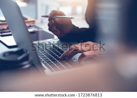 Work from home office, teleworking, online learning concept. Businessman typing on laptop computer at home. Man browsing internet at home. Student studying online class with pen, book on desk, closeup Royalty-Free Stock Photo #1723876813