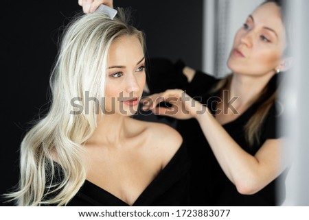 Beautiful girl surrounded by the hands of a hairstylist with a comb near her head. Photo of a happy woman.