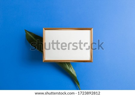 Anniversary message letter space. Empty photo frame with green leaf on blue background. top view, copy space