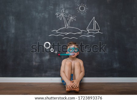 Funny little kid is dreaming about travelling. Little boy in scuba diving mask with drawn picture of palm and seaside.