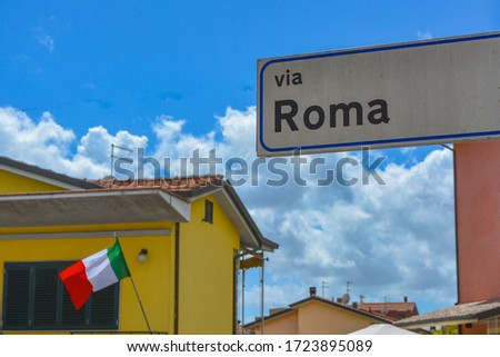 A patriotic scene from Italy: Rome street (Via Roma), the italian flag (tricolore) and a deep blue italian sky with typical mediterranean houses around. Beautiful scene for Italy's national day