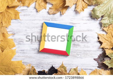 Blank rectangular photo frame lies on vintage wooden desk with bright autumn foliage. Flat lay with autumn leaves on white wooden surface. Simple colorful picture frame with copy space for design.