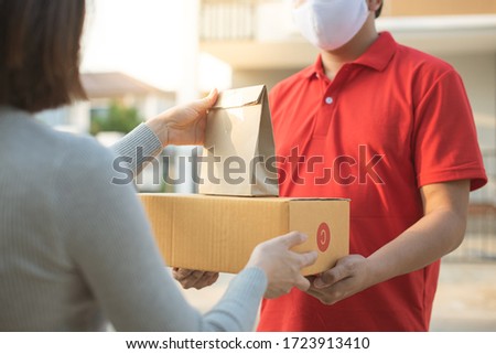 Deliver man wearing face mask in red uniform handling bag and  parcel box give to female costumer Postman and express grocery delivery service during covid19. Royalty-Free Stock Photo #1723913410