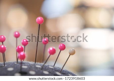 Pink pins on pincushion for sewing fabric with blurred bokeh background close-up.