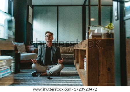 Businessman meditating in lotus pose on the floor in the office. Mature business professional doing yoga meditation in office lounge. Royalty-Free Stock Photo #1723923472