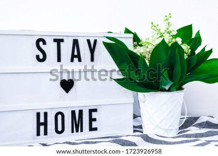 Lightbox with text STAY HOME and bouquet lilies of the valley in white bucket, spring time, quarantine, holiday background