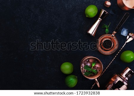 Preparation Moscow Mule cocktail with ginger beer, vodka, lime and ice. Copper bar tools. Black bar counter background. Top view. Copy space