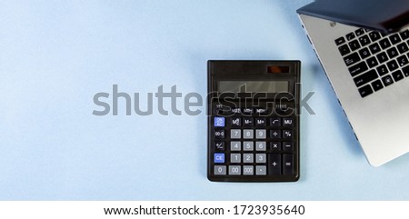 Flat lay of workspace with calculator and laptop on the blue background.