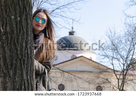 Fashionable girl posing near a tree. Spring weather, sunny day. Ancient surrender in the background.